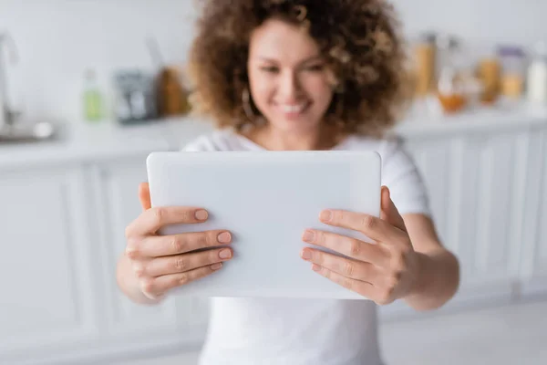 Selective focus of digital tablet in hands of smiling woman taking selfie on blurred background — Stock Photo