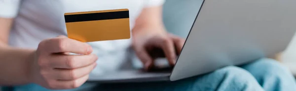 Messa a fuoco selettiva della carta di credito in mano della donna ritagliata con computer portatile su sfondo sfocato, banner — Foto stock