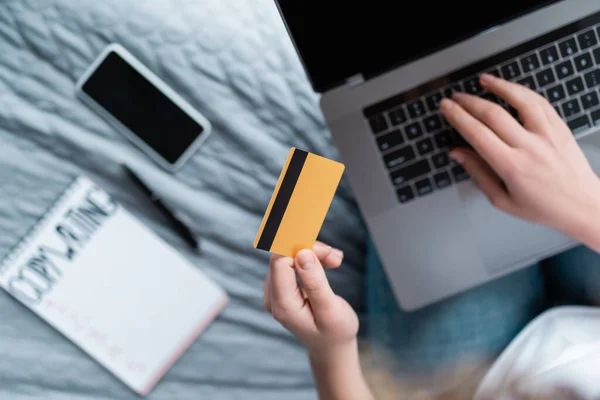 Partial view of woman with credit card using laptop near blurred notebook and smartphone — Stock Photo