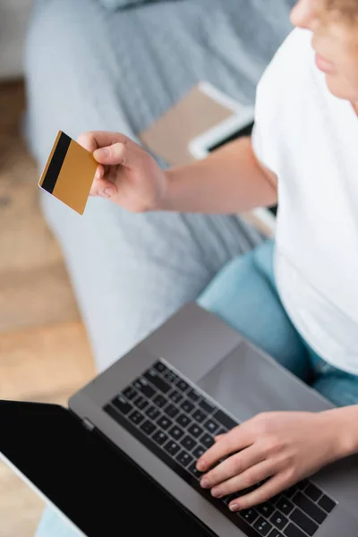 Teilansicht einer Frau mit Kreditkarte und Laptop mit leerem Bildschirm im Schlafzimmer — Stockfoto