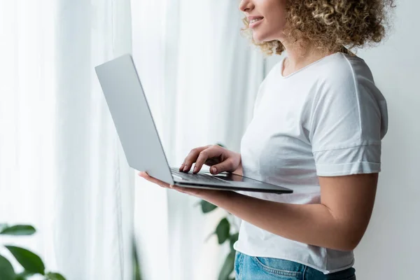 Vista parcial de la mujer sonriente usando el ordenador portátil mientras está de pie en casa — Stock Photo