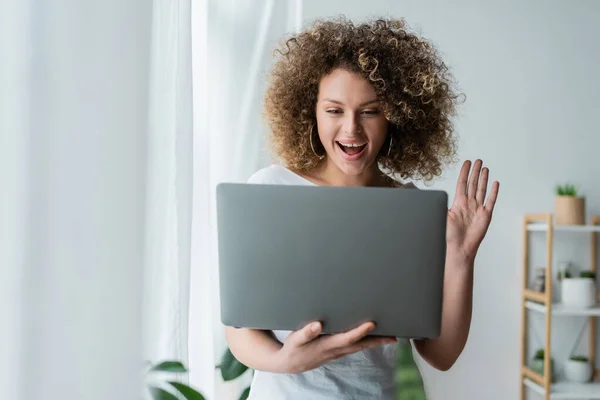 Femme étonnante et heureuse agitant la main pendant le chat vidéo sur ordinateur portable — Photo de stock
