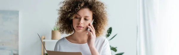 Junge, lockige Frau mit Mappe, die zu Hause mit dem Handy spricht, Banner — Stockfoto