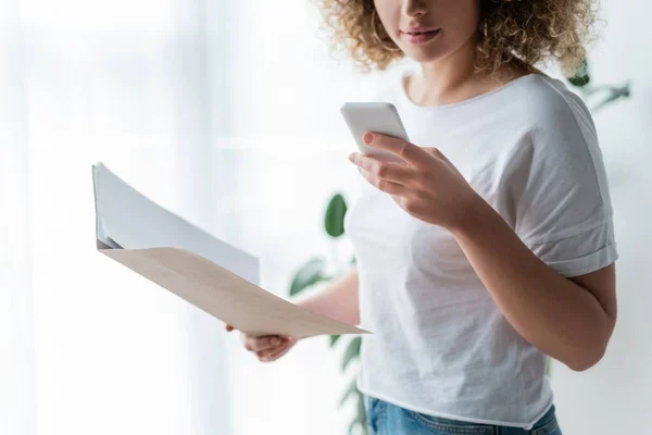 Vista recortada de la mujer con la carpeta utilizando el teléfono móvil en casa - foto de stock