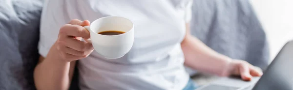 Частковий вид розмитої жінки, що тримає чашку кави вдома, банер — стокове фото