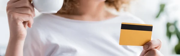 Cropped view of woman with credit card and coffee cup on blurred background, banner — Stock Photo