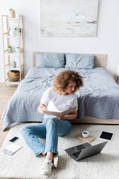 Volle Länge der Werbetexter arbeiten auf dem Boden im Schlafzimmer in der Nähe von Gadgets und Kaffeetasse — Stockfoto
