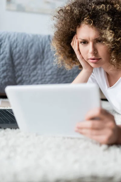 Thoughtful woman lying on floor and looking at digital tablet — Stock Photo