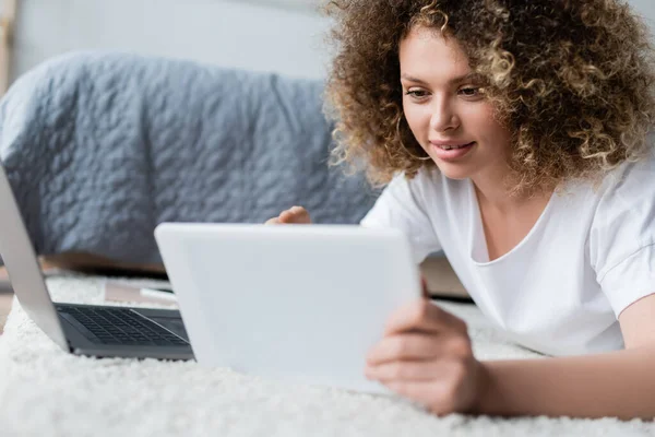Усміхнена жінка використовує цифровий планшет на підлозі біля ноутбука — стокове фото
