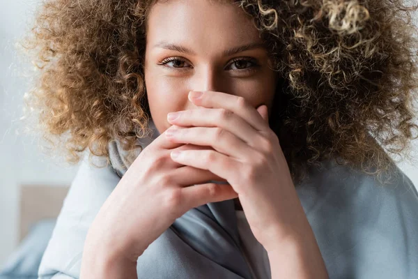Young curly woman with happy eye expression obscuring face with hands and looking at camera — Stock Photo