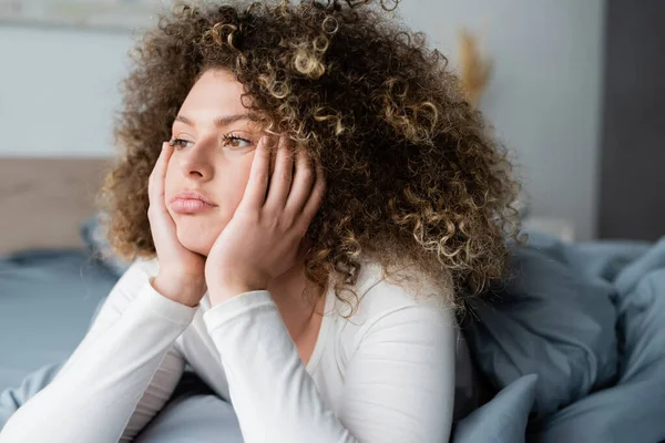 Traurige und nachdenkliche Frau mit Händen in der Nähe des Gesichts, die im Schlafzimmer wegschaut — Stockfoto