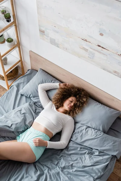 Вид сверху молодой женщины с закрытыми глазами, лежащей на кровати в белой пижаме — стоковое фото