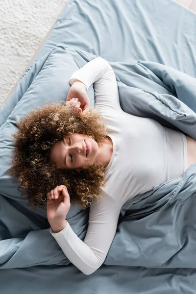 Draufsicht einer glücklichen Frau mit geschlossenen Augen, die sich morgens auf dem Bett ausstreckt — Stockfoto