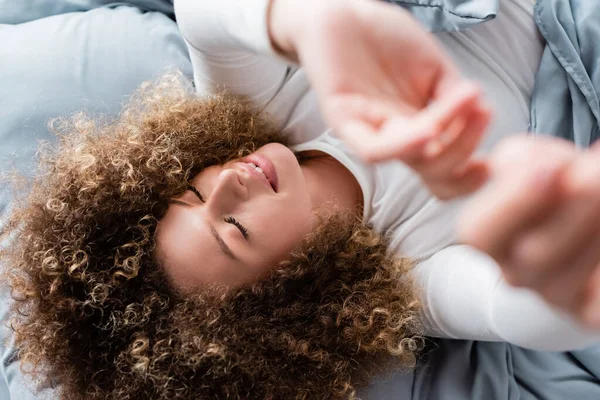 Top view of smiling curly woman lying with outstretched hands on blurred foreground — Stock Photo