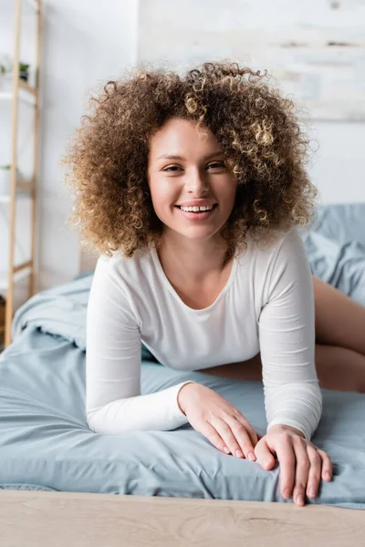 Charmante Frau mit welligem Haar lächelt auf dem heimischen Bett in die Kamera — Stockfoto