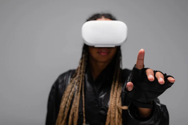 Unscharfe afrikanisch-amerikanische Frau in Virtual-Reality-Headset zeigt mit Finger isoliert auf grau — Stockfoto