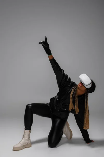 Full length of african american woman in virtual reality headset pointing with finger on grey background — Stock Photo