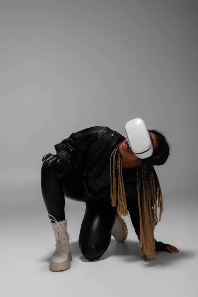 African american woman in leather jacket using virtual reality headset on grey background — Stock Photo