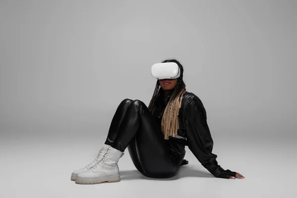 African american woman in virtual reality headset sitting on grey background — Stock Photo