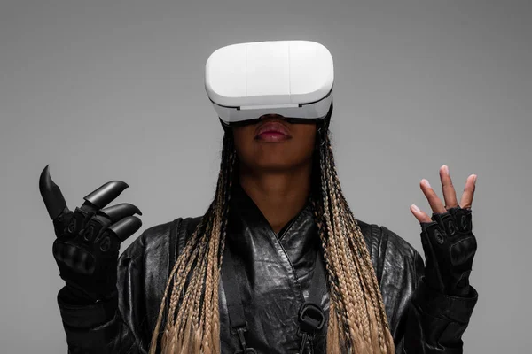 African american woman in gloves and leather jacket using virtual reality headset isolated on grey — Stock Photo