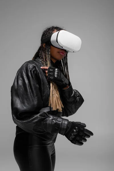 Mujer afroamericana en guantes de cuero y auriculares vr aislados en gris - foto de stock