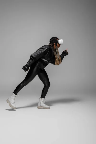 Side view of african american woman in vr headset running on grey background — Stock Photo