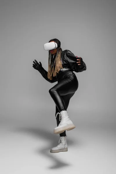 Stylish african american woman in leather jacket using vr headset on grey background — Stock Photo