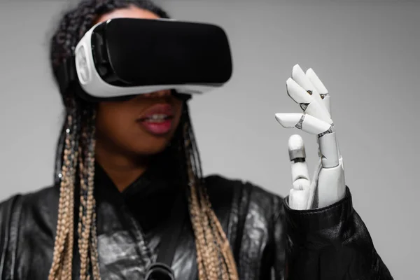 Blurred african american woman in vr headset with robotic hand isolated on grey — Stock Photo