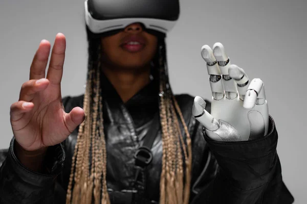 Blurred african american woman in virtual reality headset with robotic hand isolated on grey — Stock Photo