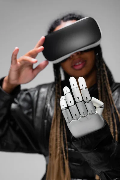 Blurred african american woman in vr headset and robotic hand isolated on grey — Stock Photo