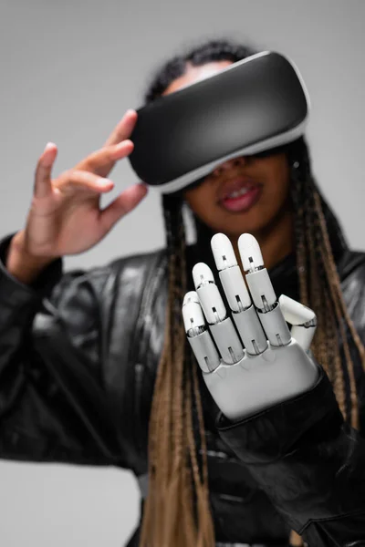 Femme afro-américaine floue en casque vr et main robotisée isolée sur gris — Photo de stock