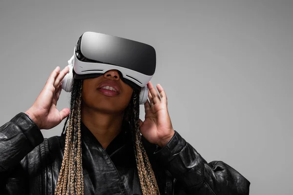 Afroamerikanerin in vr-Headset hört Musik in Kopfhörern isoliert auf grau — Stockfoto