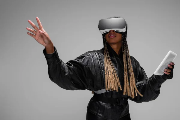 Elegante mujer afroamericana en auriculares de realidad virtual sosteniendo tableta digital aislada en gris - foto de stock