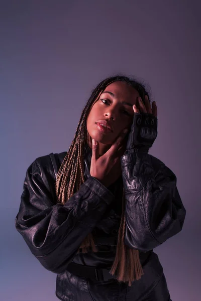 Stylish african american woman in leather jacket touching face isolated on purple — Stock Photo