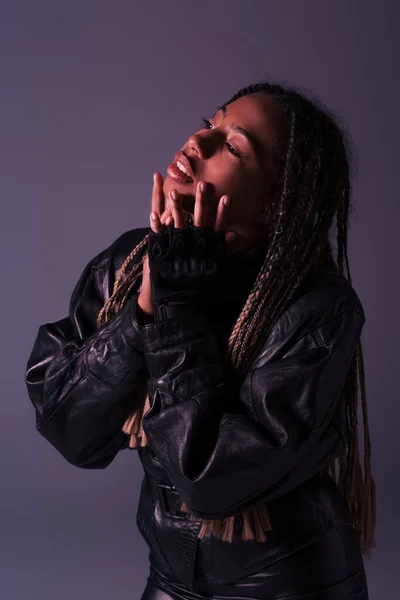 African american woman in leather jacket and glove touching face isolated on purple — Stock Photo