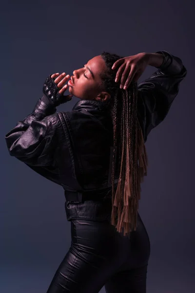 Donna afroamericana in guanto e giacca di pelle toccante trecce isolate su grigio scuro — Foto stock