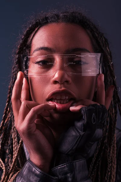 Retrato de mujer afroamericana en guante y gafas inteligentes mirando a la cámara aislada en gris oscuro - foto de stock