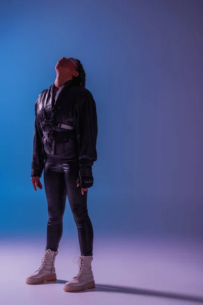 Pleine longueur de femme afro-américaine élégante dans des lunettes intelligentes debout sur fond bleu et violet — Photo de stock