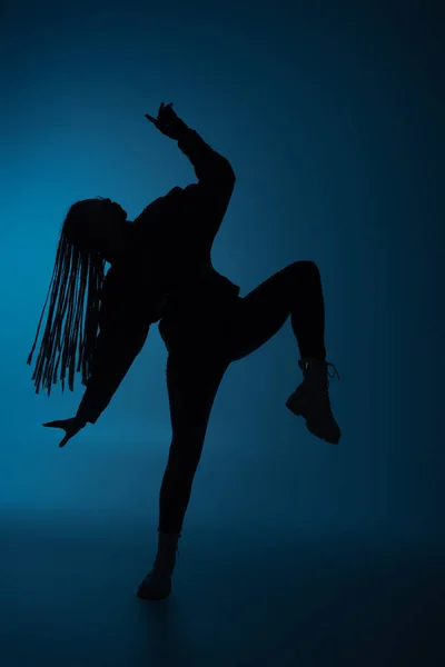 Side view of silhouette of african american woman moving on dark blue background — Stock Photo