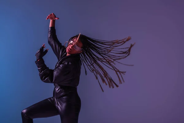 Mulher americana africana elegante em luva e óculos inteligentes se movendo em fundo azul e roxo — Fotografia de Stock