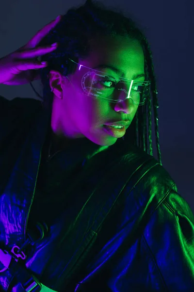 Portrait de femme afro-américaine élégante dans des lunettes intelligentes regardant loin isolé sur bleu foncé — Photo de stock