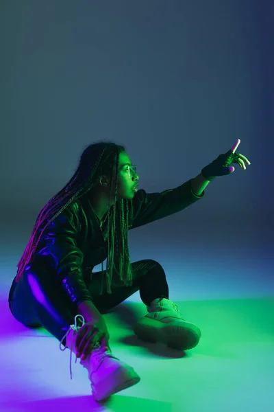 Side view of african american woman in smart glasses pointing with finger on blue background with lighting — Stock Photo