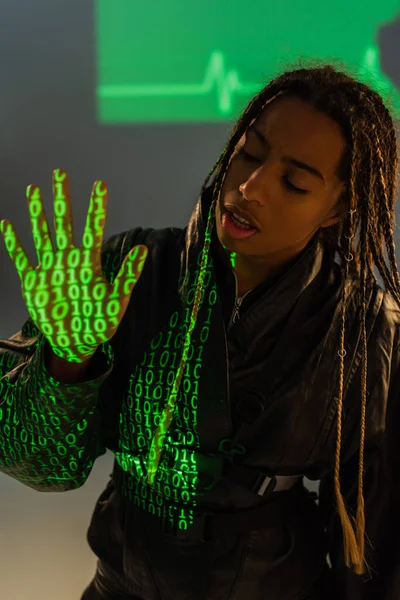 Mulher afro-americana em jaqueta de couro com projeção de código de computador em fundo cinza — Fotografia de Stock