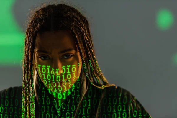 Porträt einer afrikanisch-amerikanischen Frau mit Projektion eines Binärcodes vor Kamera auf grauem Hintergrund — Stockfoto