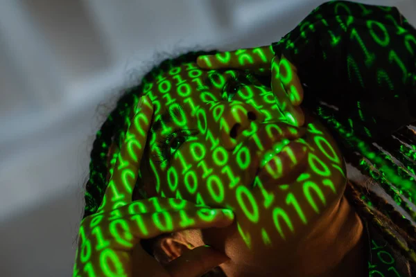 Low angle view of african american woman with projection of binary code touching face on grey background — Stock Photo