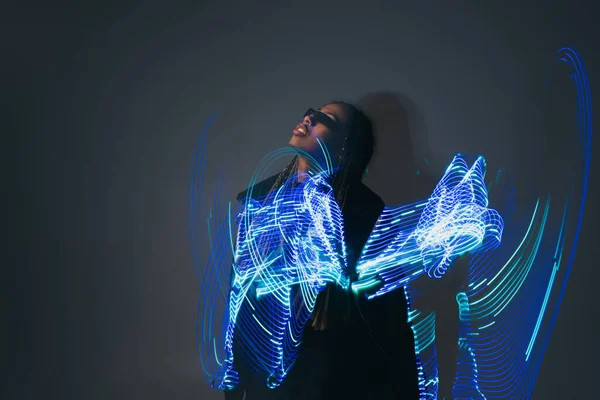 African american woman in smart glasses standing near abstract projection on grey background — Stock Photo