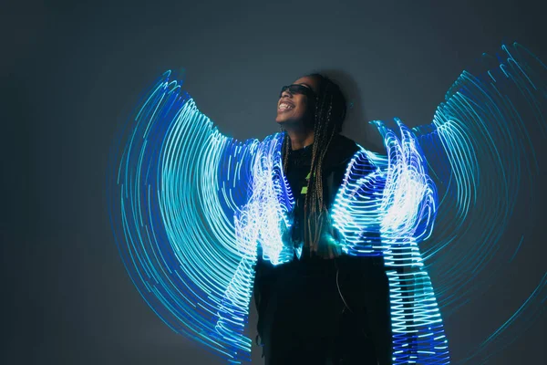 Femme afro-américaine souriante en lunettes intelligentes avec projection abstraite sur fond gris — Photo de stock