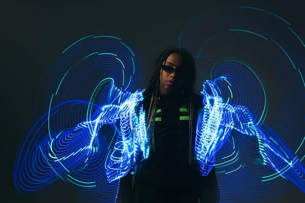 Mujer afroamericana en gafas inteligentes de pie cerca de luces de neón sobre fondo gris - foto de stock