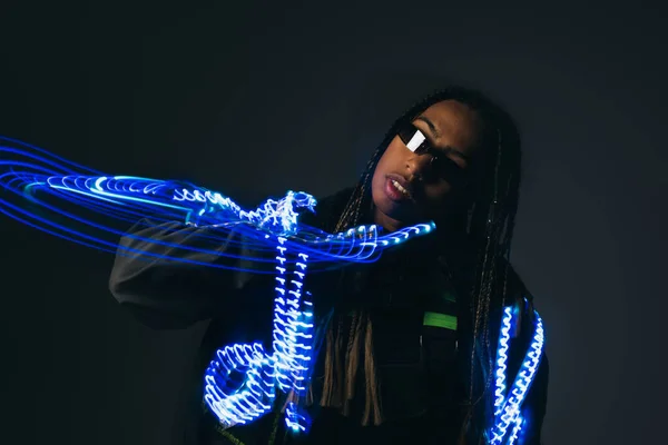 Femme afro-américaine en lunettes intelligentes debout près des néons bleus sur fond gris — Photo de stock