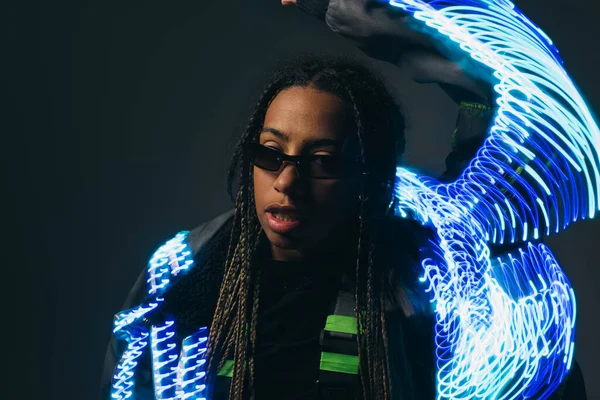 Femme afro-américaine en lunettes intelligentes posant près de néons sur fond gris — Photo de stock